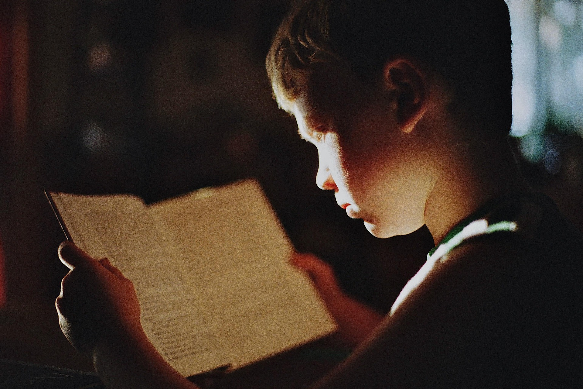 A boy reading a book by lamplight, deeply focused