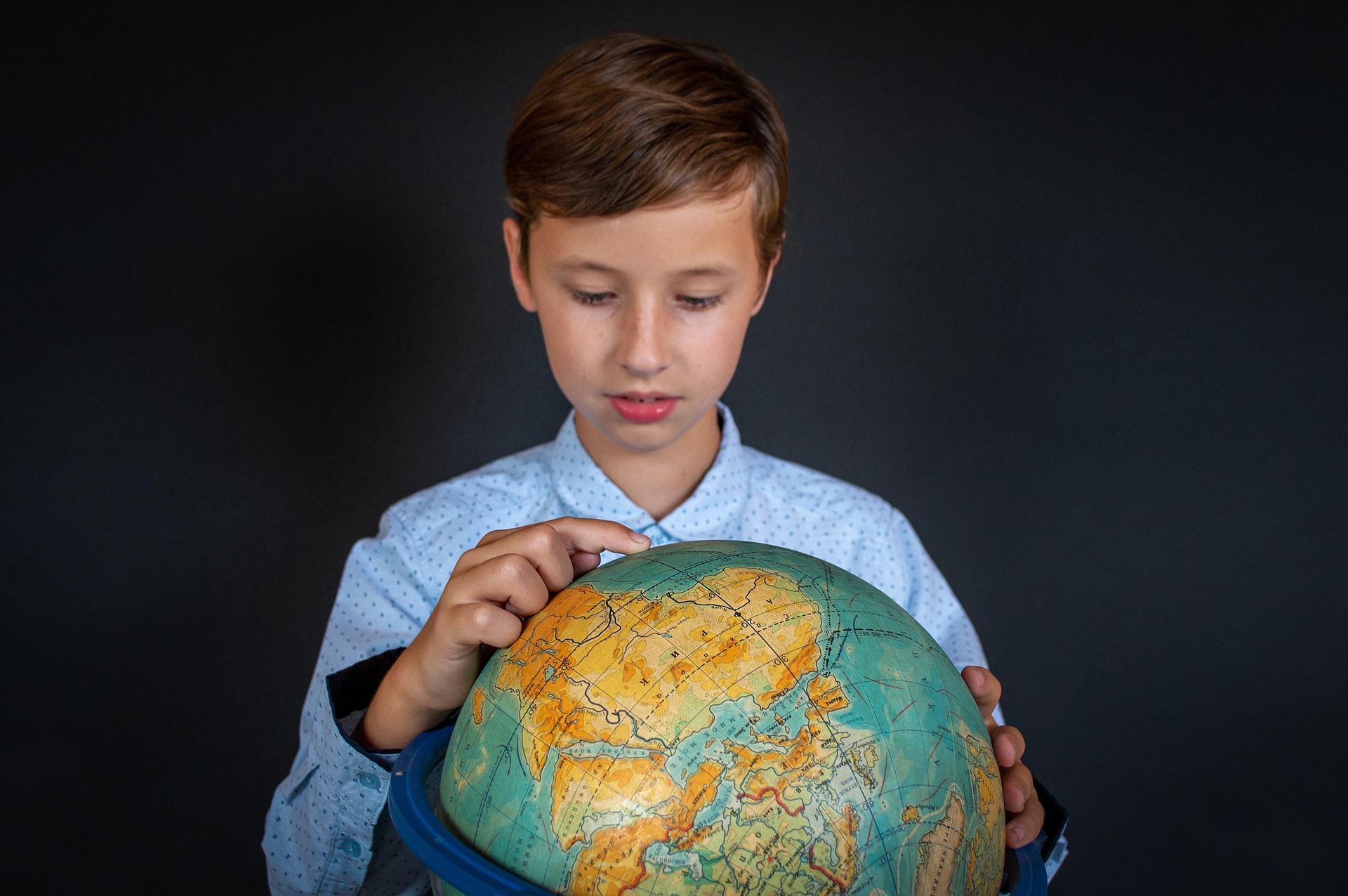 A young student holding a globe, tracing a route
